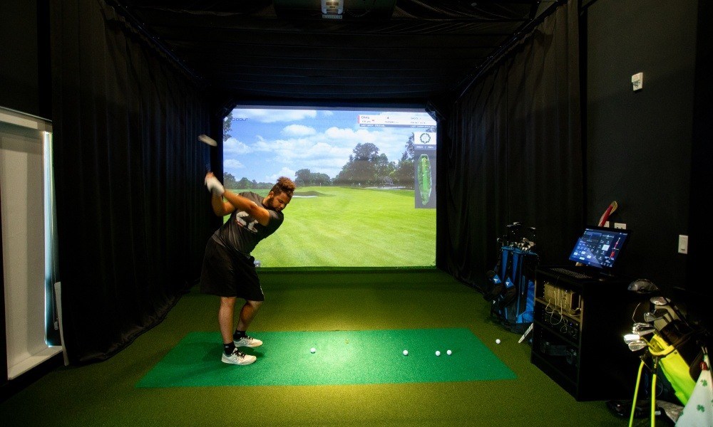 A man is playing golf indoors on a green mat.