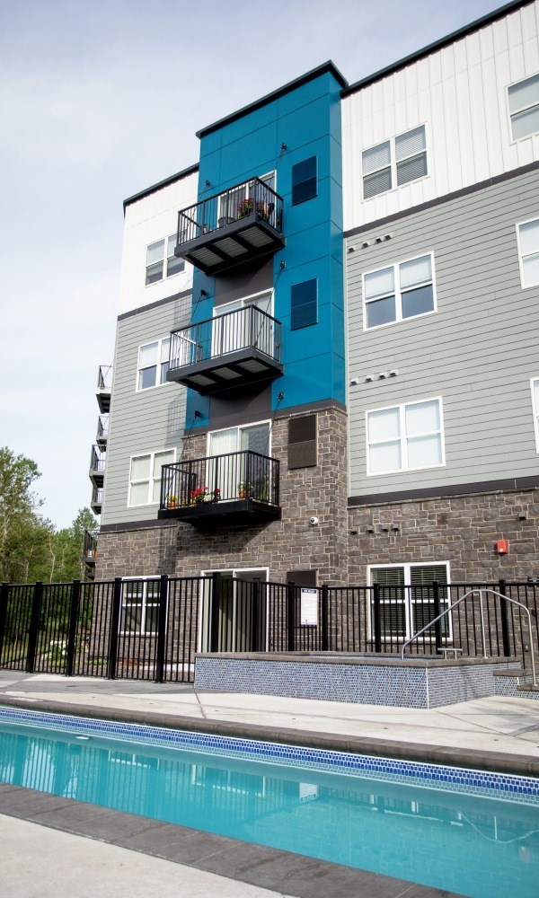 A blue and grey apartment building with a pool in front.