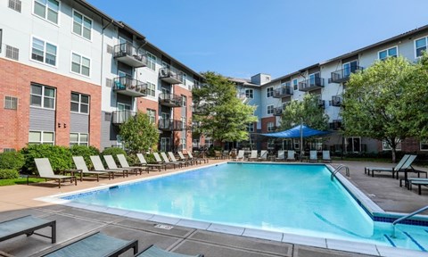 A swimming pool surrounded by lounge chairs and apartment buildings.