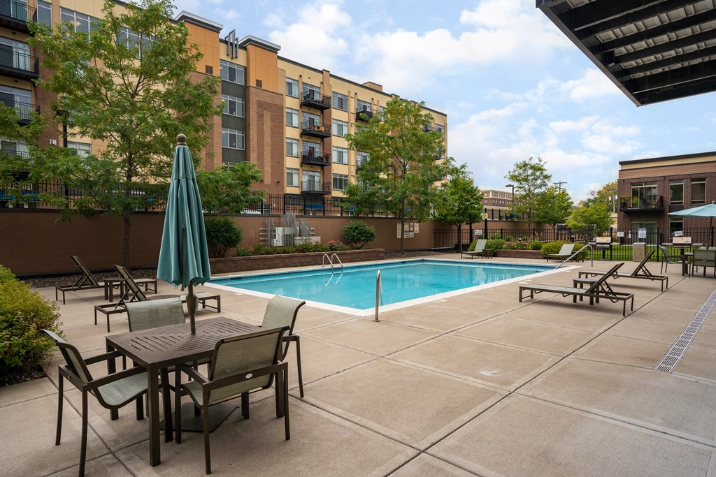 a swimming pool with tables and chairs in front of an apartment building