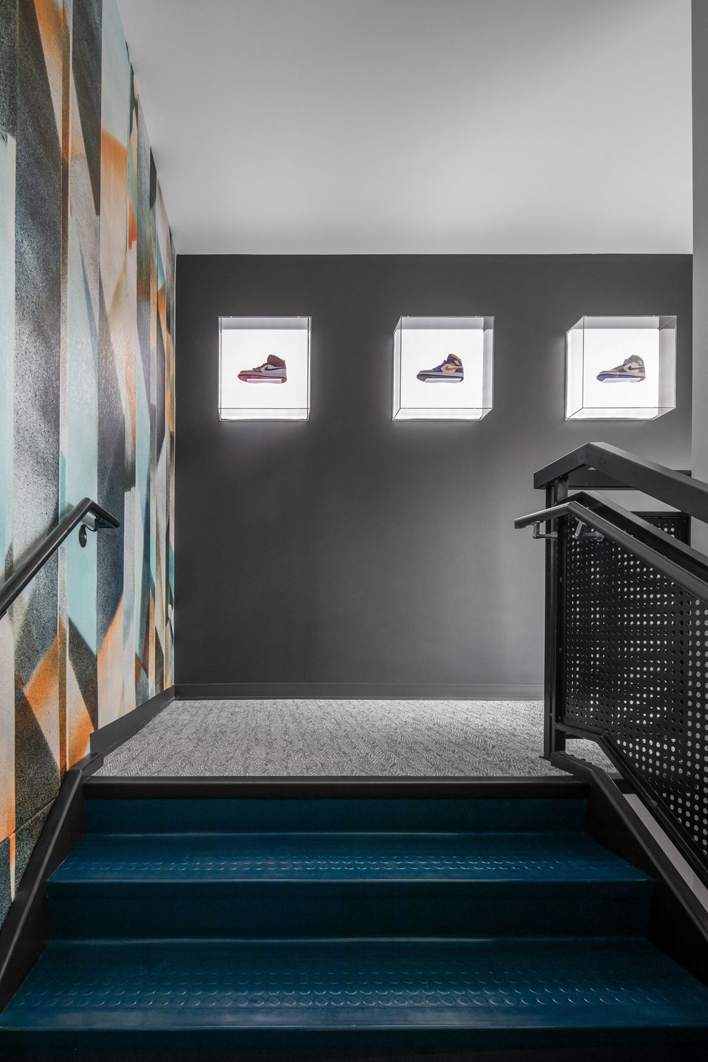 a staircase with a blue carpet and a wall with three sneakers on it