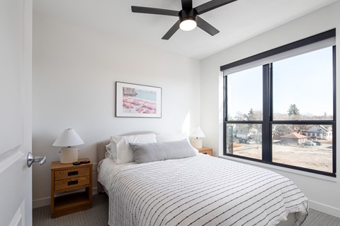 a bedroom with a bed and a ceiling fan and a large window