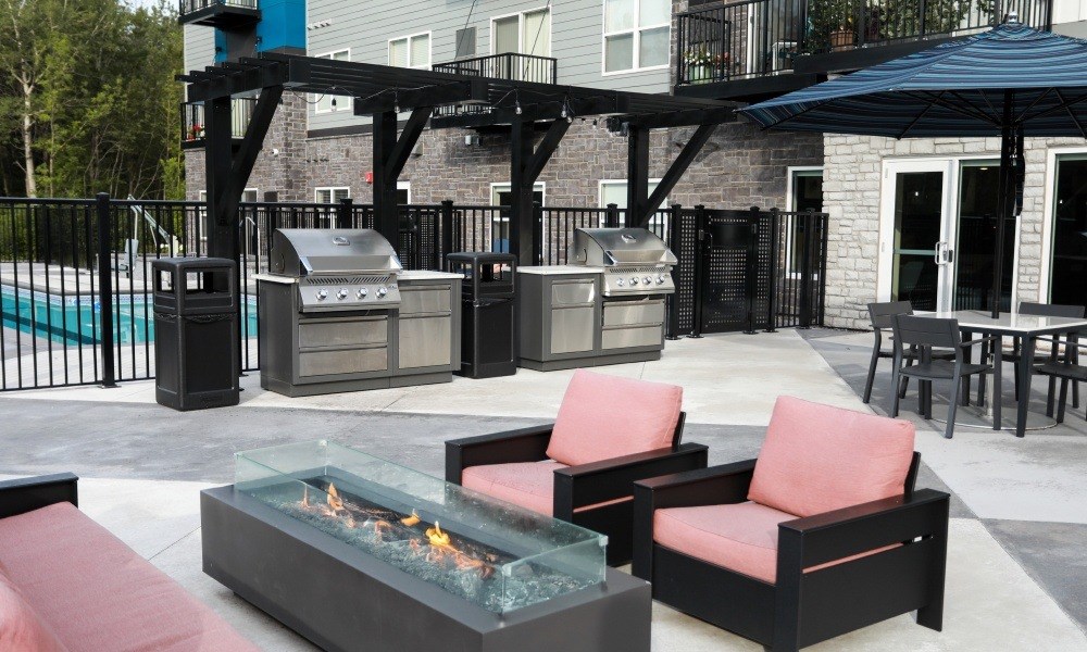 A patio with a fire pit, chairs, and a grill.