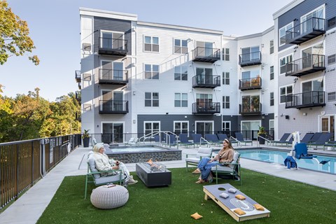 two people sitting in lawn chairs near a swimming pool in front of an apartment building