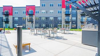 A patio with tables and chairs is in front of a grey building with red accents.