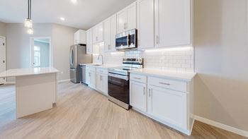 A modern kitchen with white cabinets and a wooden floor.