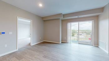 A spacious room with light wood flooring and a sliding glass door leading to a balcony.