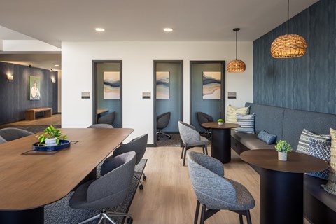 A modern coworking lounge with a wooden table and grey chairs.