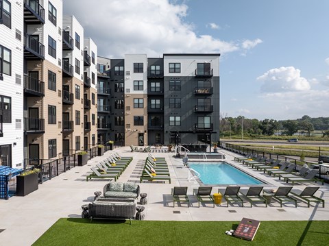 A large outdoor pool area with sun loungers and a hot tub in front of a modern apartment block.