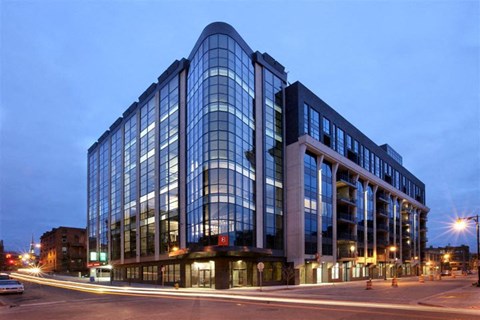 A modern glass building is illuminated at dusk.