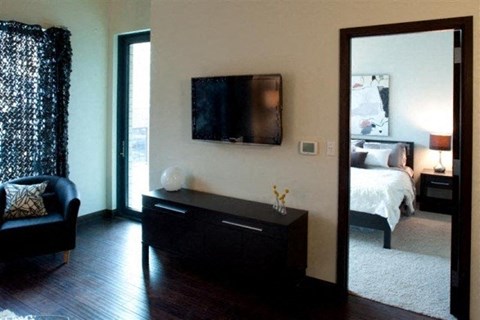 A black sofa sits in a living room with a television mounted on the wall.