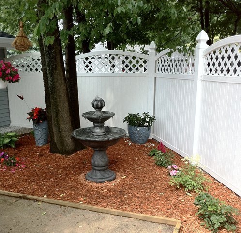 a garden with a fountain in front of a white fence