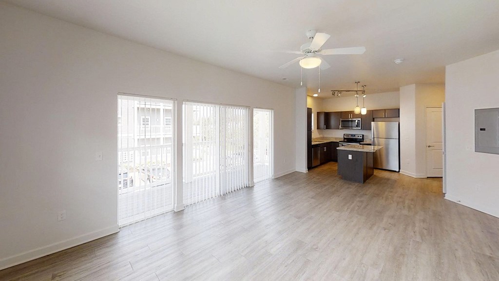 an empty living room with a kitchen and a ceiling fan