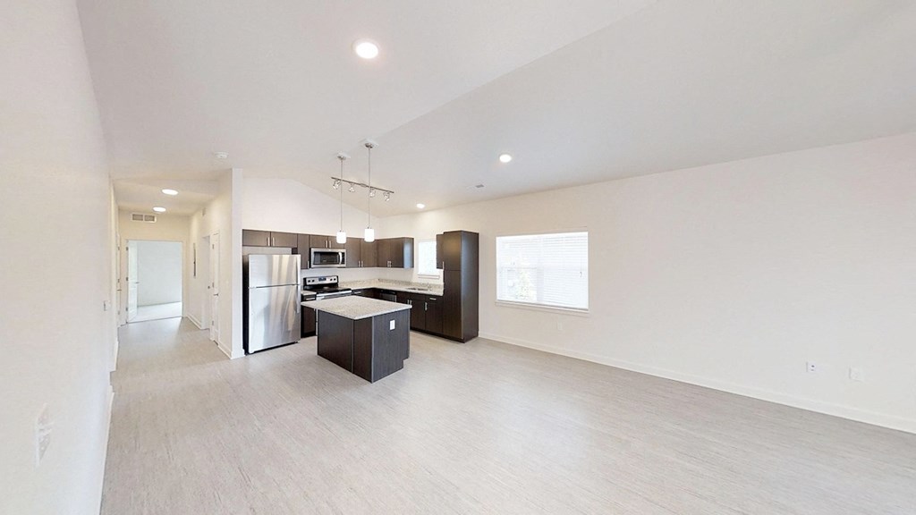 an empty living room and kitchen with a refrigerator and a sink
