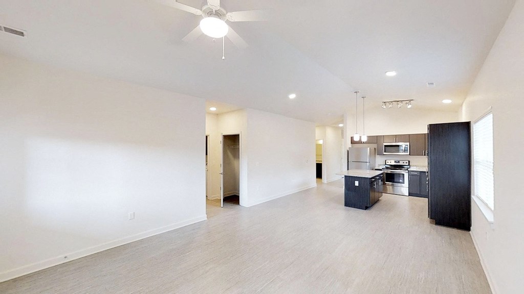 an empty living room with a kitchen and a ceiling fan