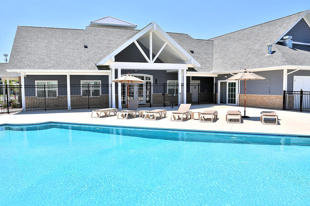 a large swimming pool in front of a building with chairs and umbrellas