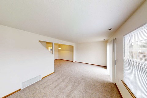 A spacious room with a carpeted floor and a window with blinds.
