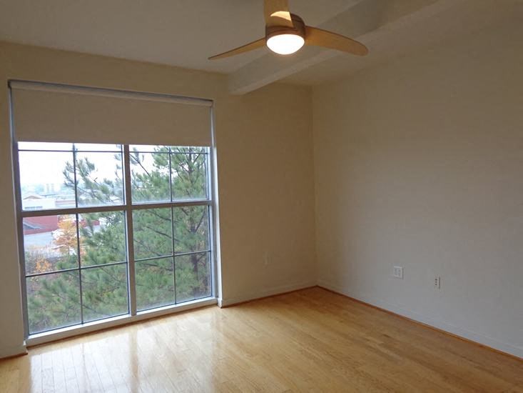 an empty living room with a large window and a ceiling fan