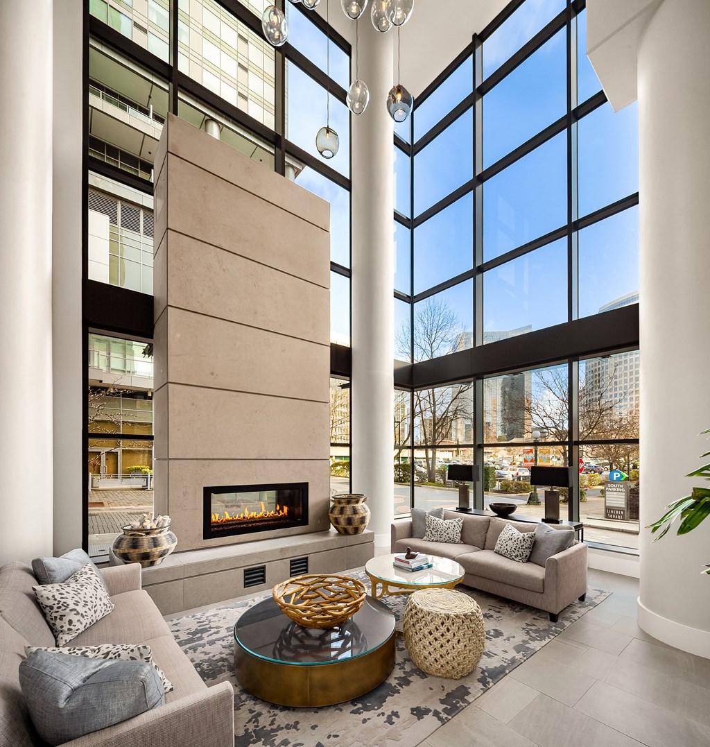 a living room with couches and a fireplace in front of tall windows at Two Lincoln Tower, Bellevue, 98004