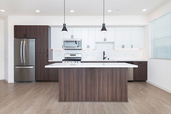Penthouse kitchen with stainless steel appliances, gas range, white quartz counters, large kitchen island, pendant lighting, and wood style flooring.