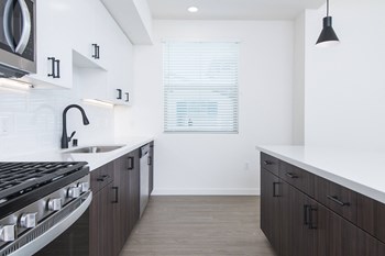 Penthouse kitchen with stainless steel appliances, gas range, white quartz counters, large kitchen island, pendant lighting, two-tone cabinetry, and wood style flooring.
