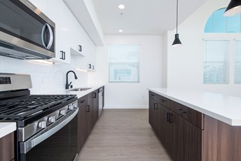 Penthouse kitchen with stainless steel appliances, gas range, white quartz counters, large kitchen island, pendant lighting, two-tone cabinetry, and wood style flooring.