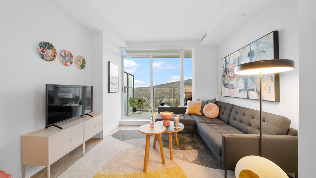 A living room with a grey couch, a wooden table, a television, and a large window.