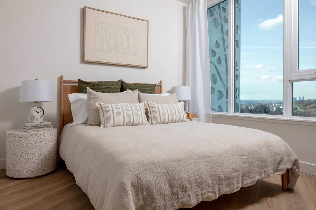 A bedroom with a large bed, a nightstand with a lamp, and a framed picture on the wall.