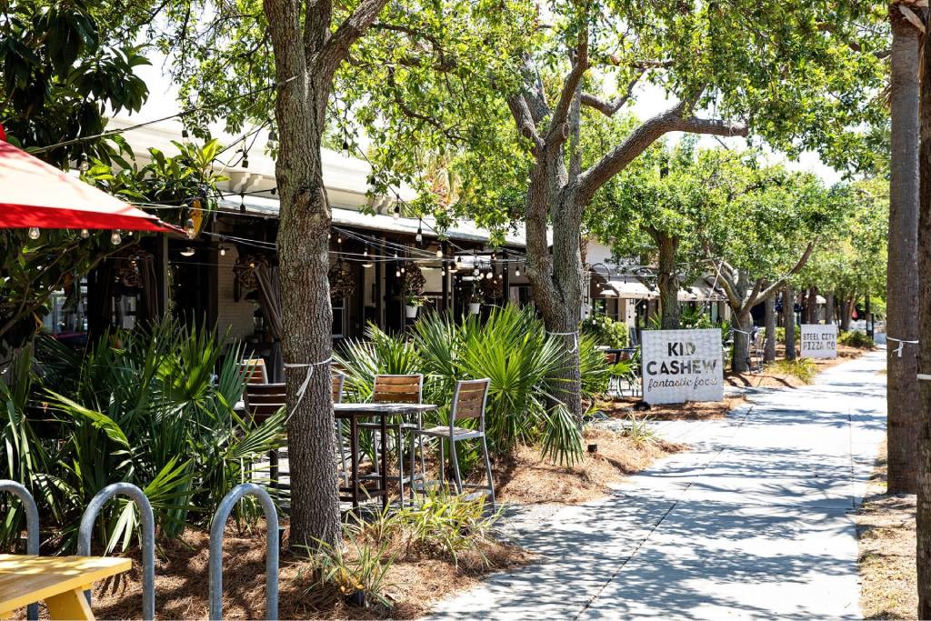 A tree-lined street with tables and chairs outside a restaurant.