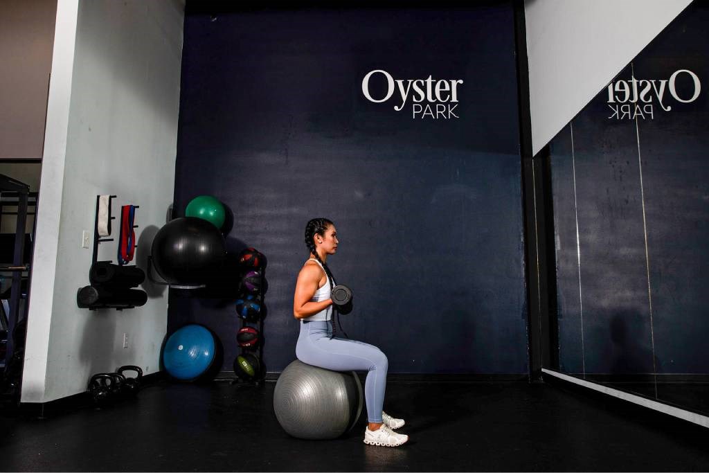 A woman is sitting on a fitness ball in a gym.