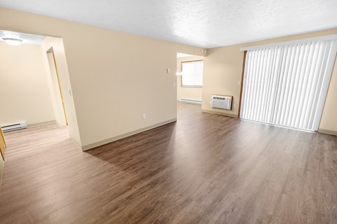 A spacious room with wooden flooring and a window with blinds.