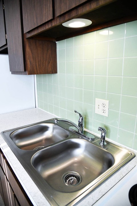 a stainless steel sink in a kitchen with green tiles