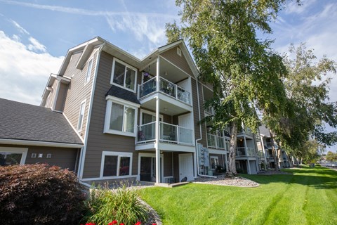 A large apartment building with a balcony and a tree in front.