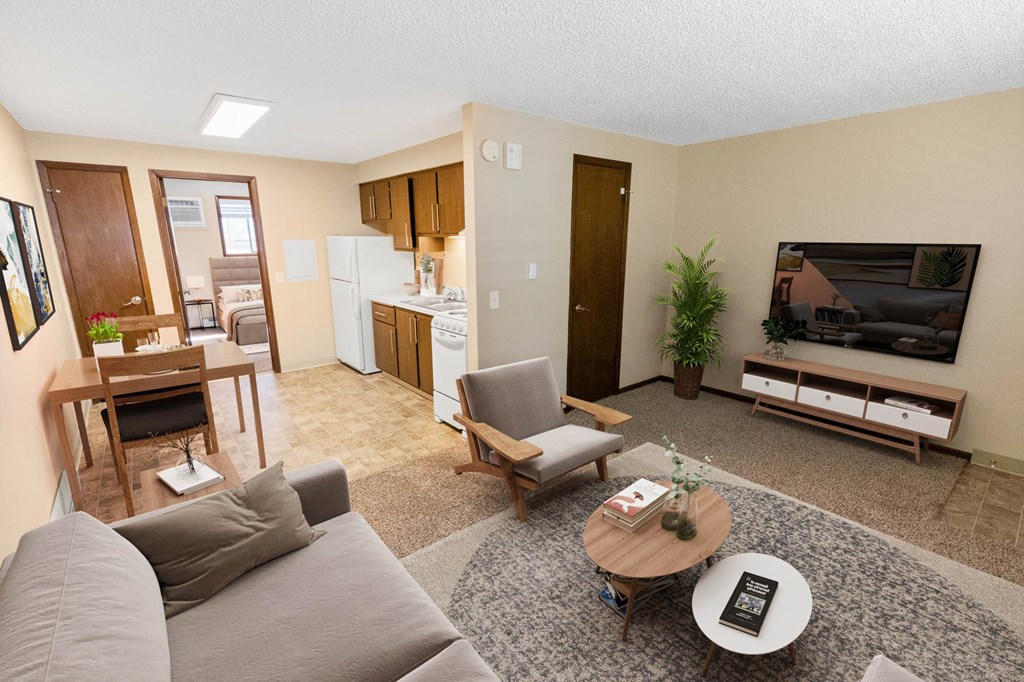 A living room with a grey couch, a coffee table, a dining table, a refrigerator, a television, and a potted plant.