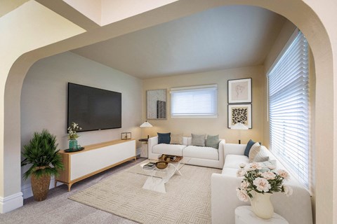 A living room with a white couch and a flat screen TV mounted on the wall.