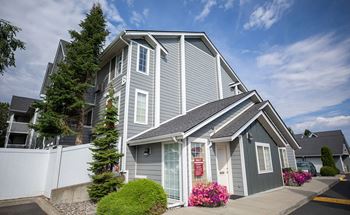 A grey house with a white fence at Morning Glory Circle Apartments, Washington, 99208 and a tree in front.