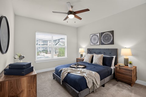 A bedroom with a large bed, a ceiling fan, and a window with a view of a cityscape.