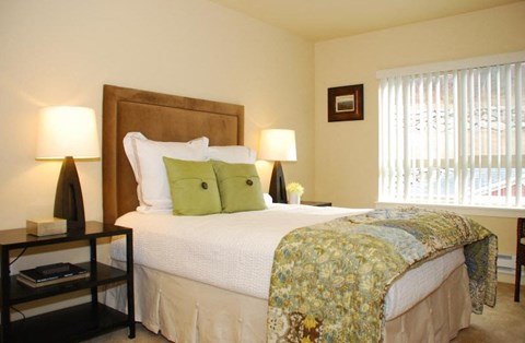 A bedroom with a large bed and a window with blinds.