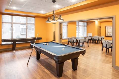 A pool table is in the middle of a room with chairs and a bench.