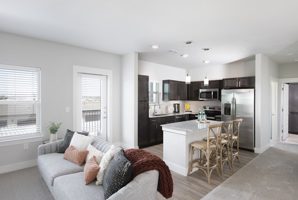 A modern kitchen with a grey couch and wooden chairs.