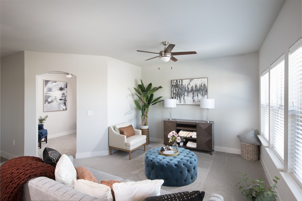 A living room with a white couch, a blue ottoman, and a ceiling fan.