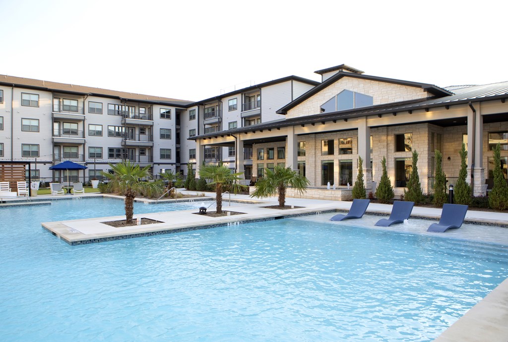 A swimming pool in front of a building with a blue umbrella.