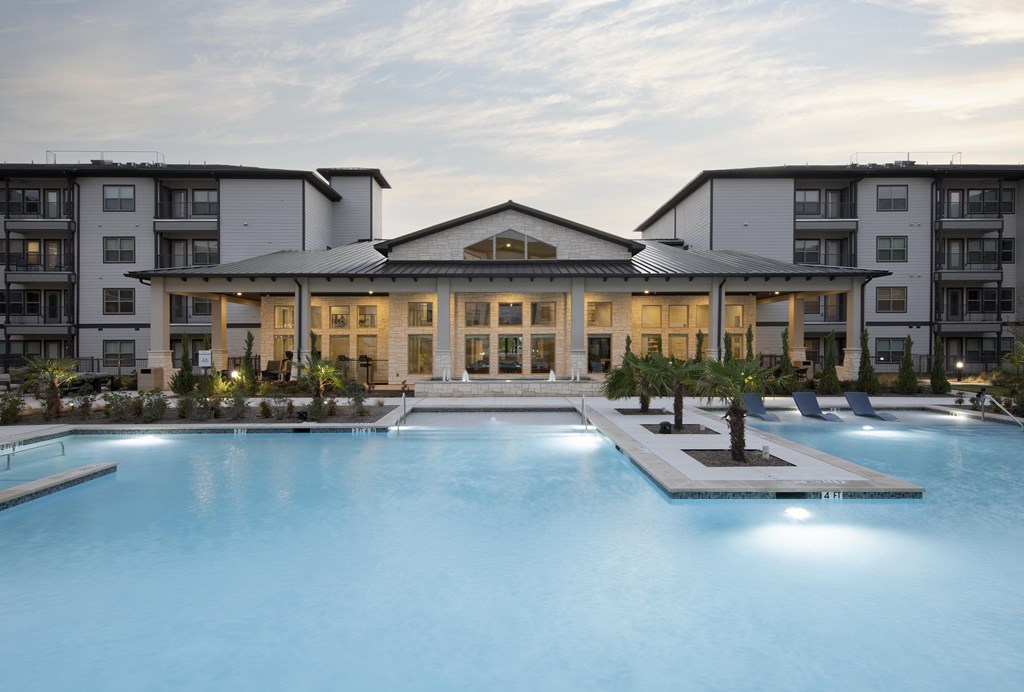 A large swimming pool in front of a building with a spacious deck and lounge chairs.