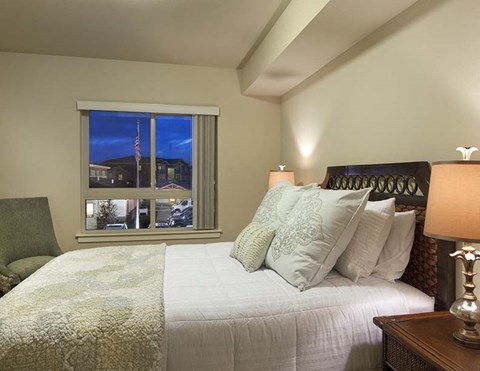 A bedroom with a bed, a chair, and a window overlooking a street.