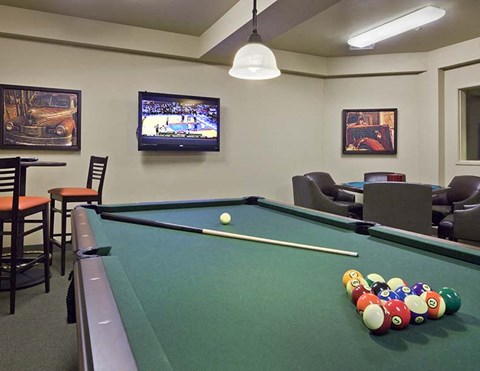 A pool table with a sports game on television in the background.