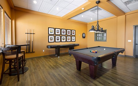 A pool table is in the middle of a room with a wooden floor and a light brown wall.