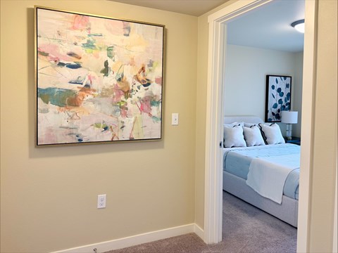 A painting hangs on a wall above a bed in a bedroom.