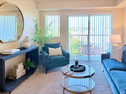 A living room with a blue couch, a coffee table, and a large window with blinds.