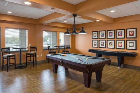 A pool table in a room with a bar and chairs.