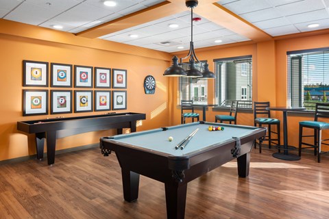 A pool table is in the middle of a room with a bar and framed pictures on the wall.